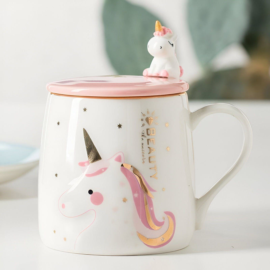 Une tasse en céramique blanche avec un couvercle rose. Sur le couvercle, il y a une figurine de licorne en céramique rose et blanche. La tasse est décorée de motifs de licornes et d'étoiles.