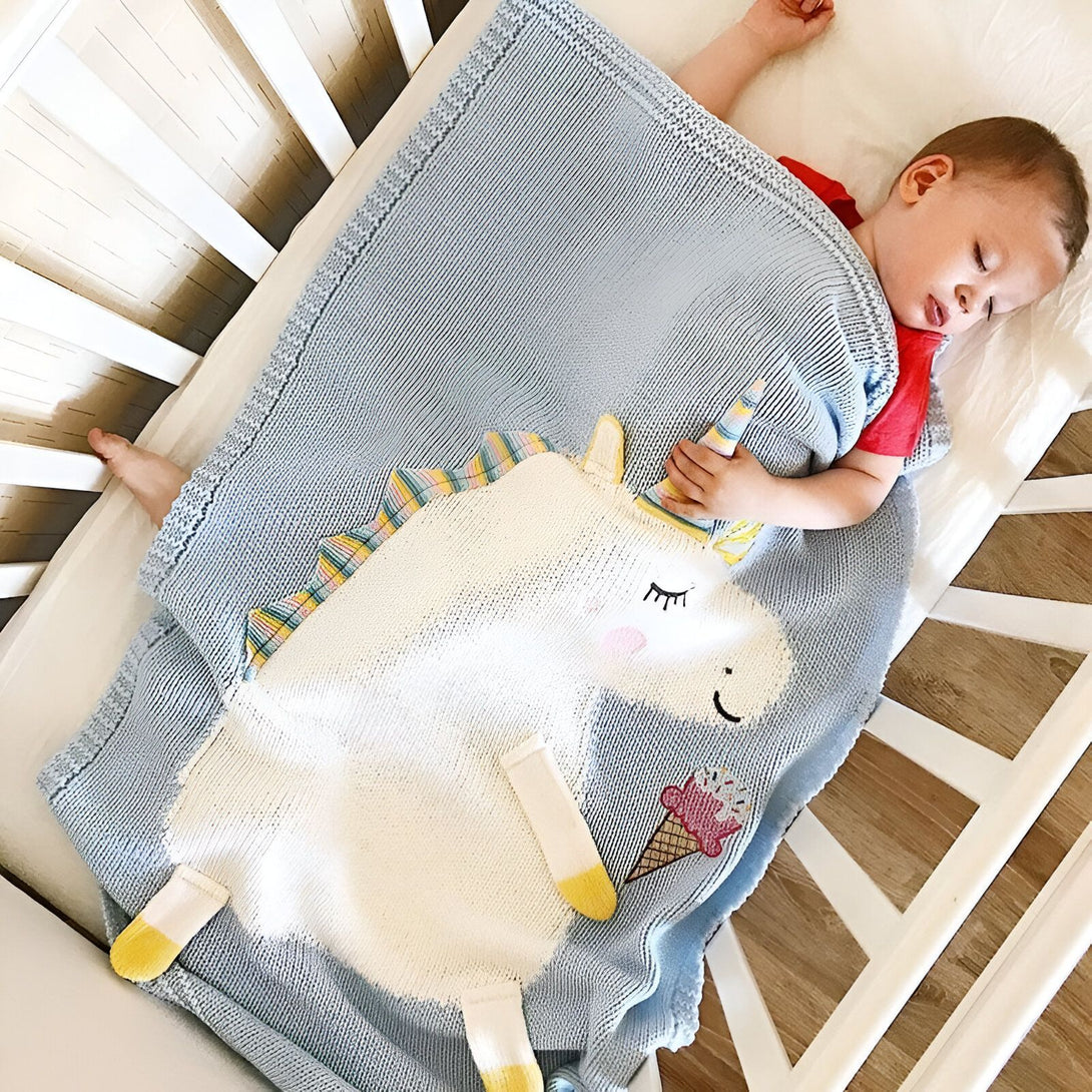 Un bébé dort dans un lit d'enfant, enroulé dans une couverture bleue avec une peluche licorne., 45501129326847,45501129359615,45501129392383,45501129425151,45501129457919,45501129490687,45501129523455,45501129556223,45501129588991,45501129621759,45501129654527,45501129687295,45501129720063 | Licorne Shop