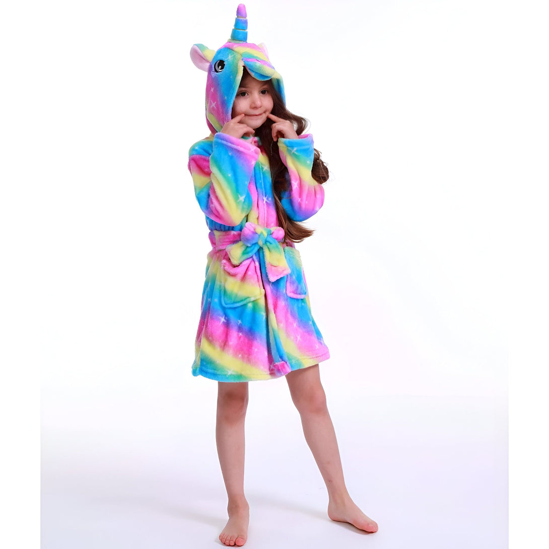 Une jeune fille porte une robe de chambre licorne arc-en-ciel à capuche. Elle a les cheveux longs et bruns et sourit à la caméra.