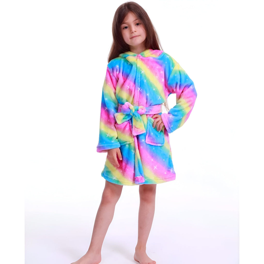 Une jeune fille porte une robe de chambre arc-en-ciel à capuche. La robe de chambre est en peluche et a des étoiles blanches. La jeune fille a les cheveux bruns et les yeux marron. Elle est pieds nus et se tient debout sur un fond blanc.