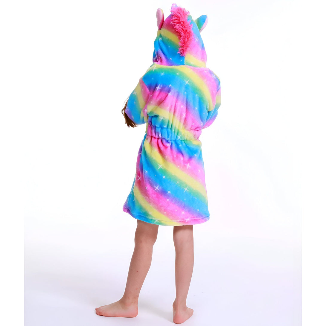 Une jeune fille porte une robe de chambre licorne arc-en-ciel avec une capuche. La robe de chambre est en peluche et a des étoiles et des lunes imprimées. La capuche a une crinière rose et une corne.