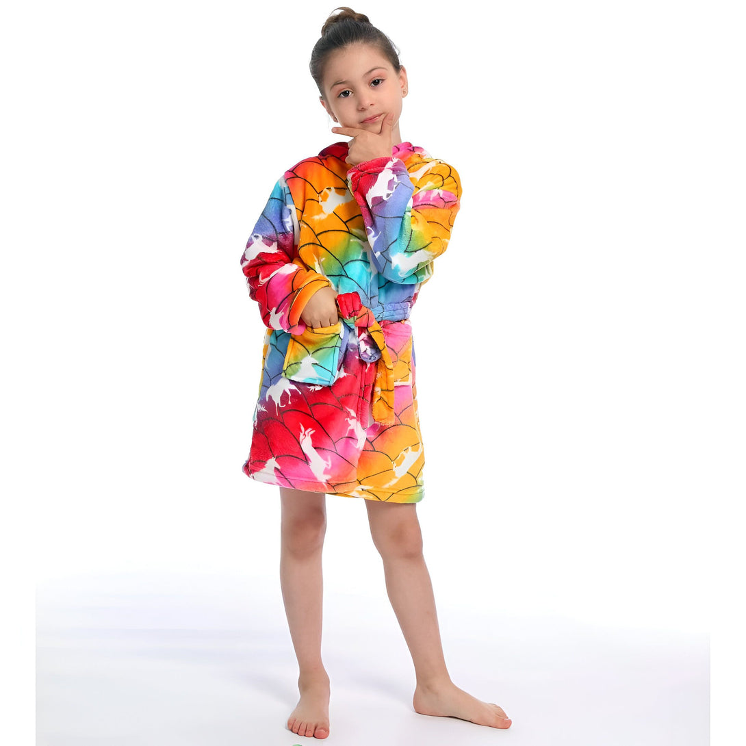 Une jeune fille porte une robe de chambre à capuche arc-en-ciel avec des licornes. Elle est debout sur un fond blanc et a l'air heureuse.