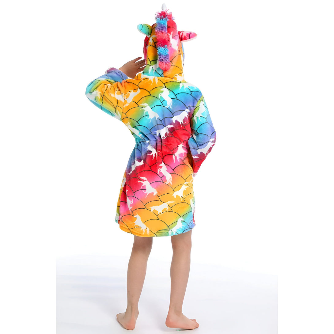 Une jeune fille porte une robe de chambre licorne arc-en-ciel à capuche. La robe de chambre est en peluche et a une longue fermeture éclair sur le devant. La capuche est doublée de polaire et a une crinière et une queue de licorne en peluche. La robe de chambre est également dotée de deux poches latérales.