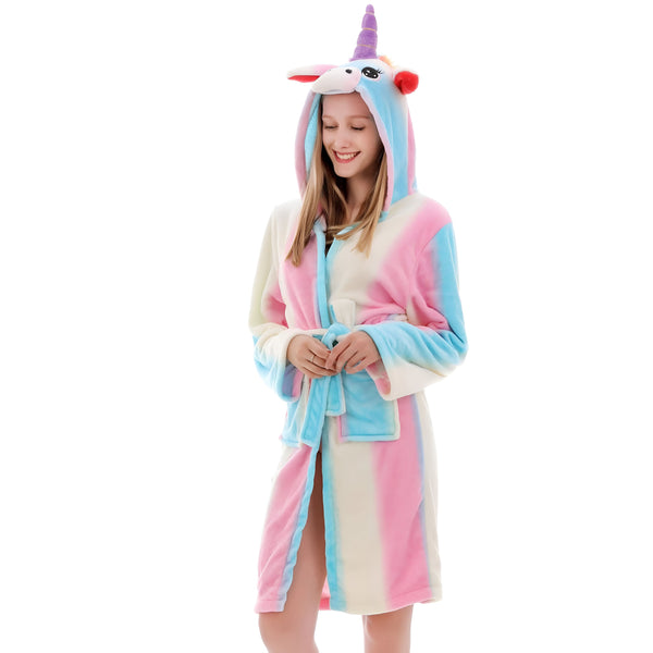 Une jeune femme porte un peignoir licorne à capuche. Le peignoir est rose, bleu et blanc. La capuche est en forme de tête de licorne avec une corne et des oreilles. La femme est souriante et a les cheveux longs et blonds.