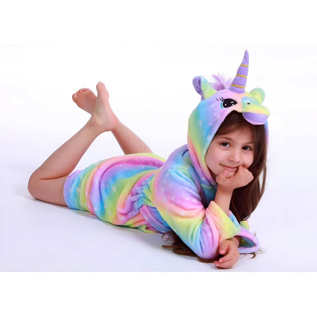 Une jeune fille porte une combinaison pyjama licorne arc-en-ciel avec une capuche. Elle est allongée sur le ventre, la tête reposant sur sa main droite. Ses pieds sont croisés derrière elle.