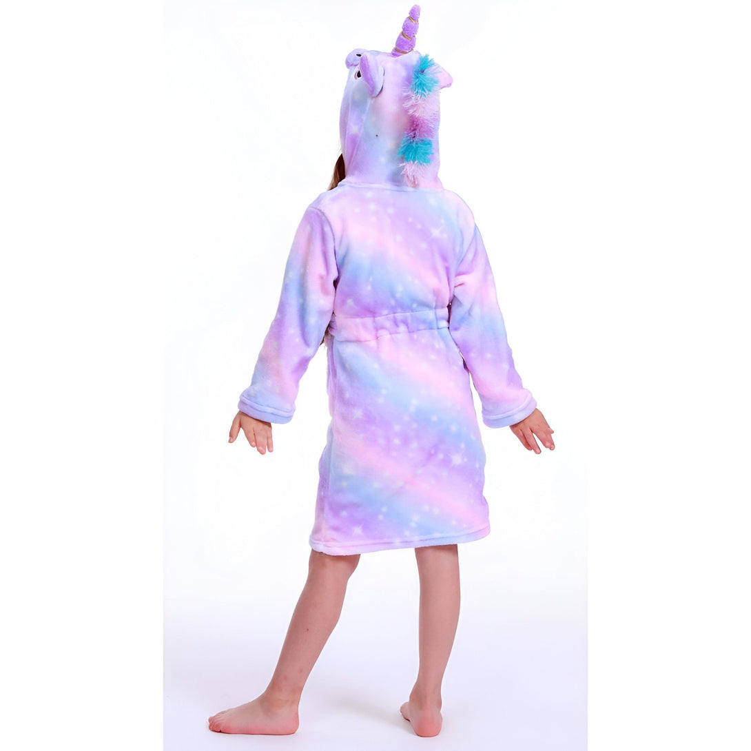 Une jeune fille porte une robe de chambre licorne violette et rose avec une capuche. La robe de chambre est en peluche et a des étoiles et des lunes imprimées. La capuche est en forme de tête de licorne avec une corne et des oreilles.