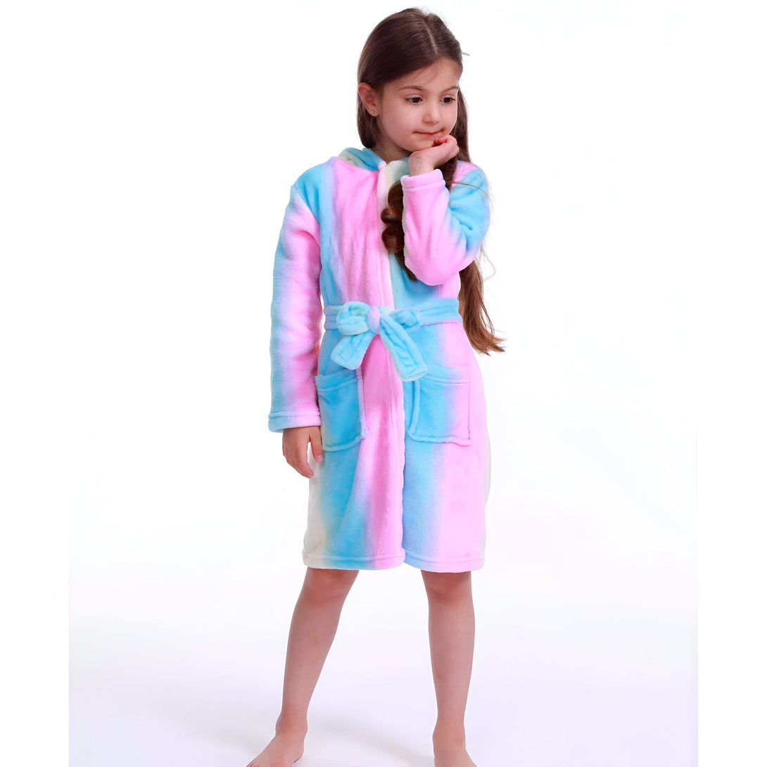 Une jeune fille porte une robe de chambre à capuche arc-en-ciel. La robe de chambre est rose, bleue et violette. La fille a les cheveux bruns et les yeux marrons. Elle est pieds nus.