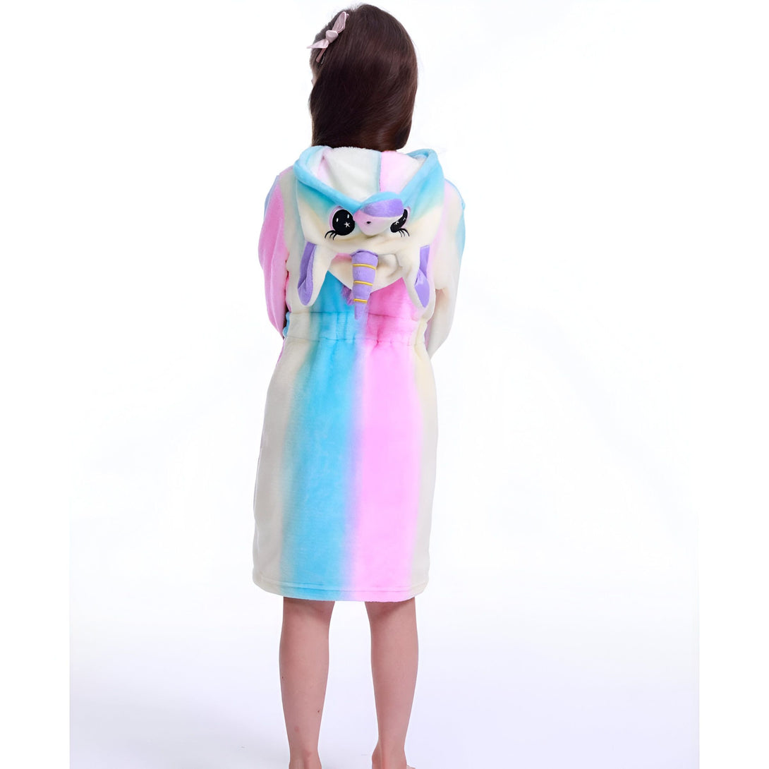Une jeune fille porte une combinaison pyjama licorne à capuche. La combinaison est rose, bleue et violette avec une capuche en forme de tête de licorne.
