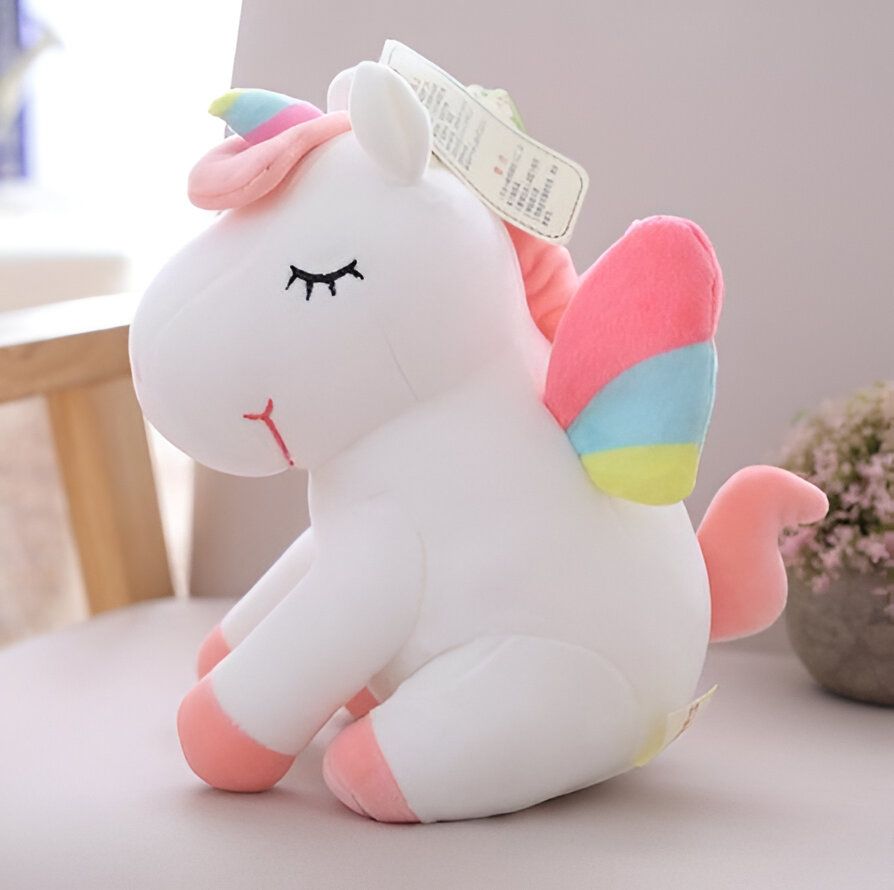 Une peluche licorne blanche avec des ailes arc-en-ciel et une corne rose.