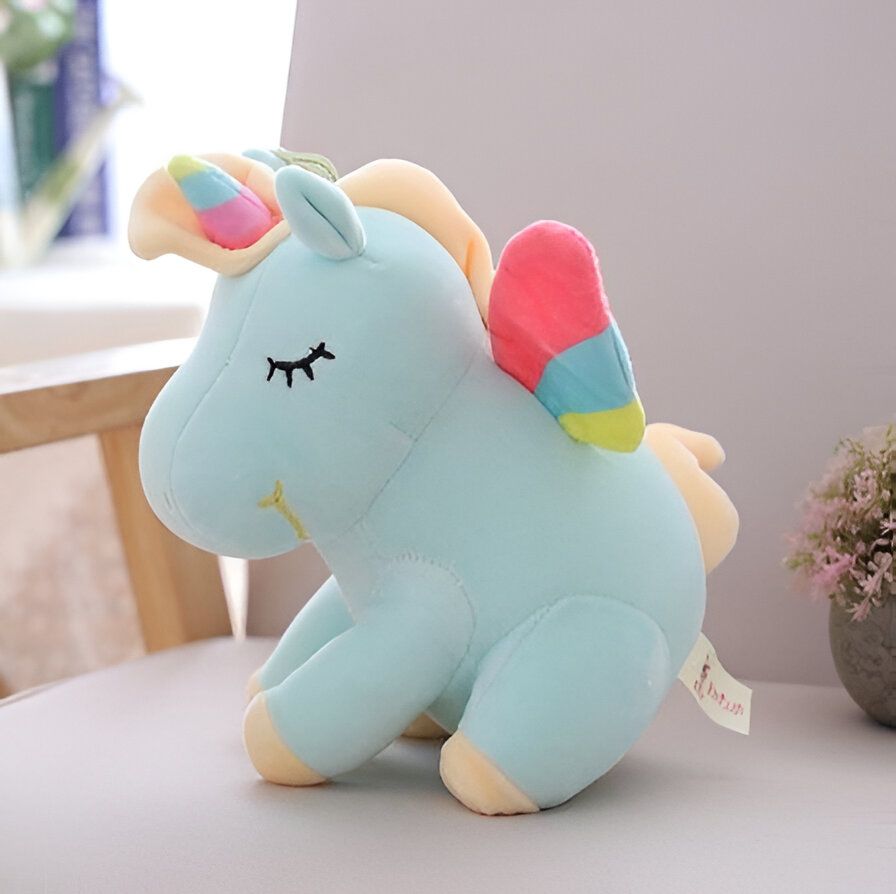 Une peluche licorne bleue avec une crinière et une queue arc-en-ciel, des ailes multicolores et une corne dorée.