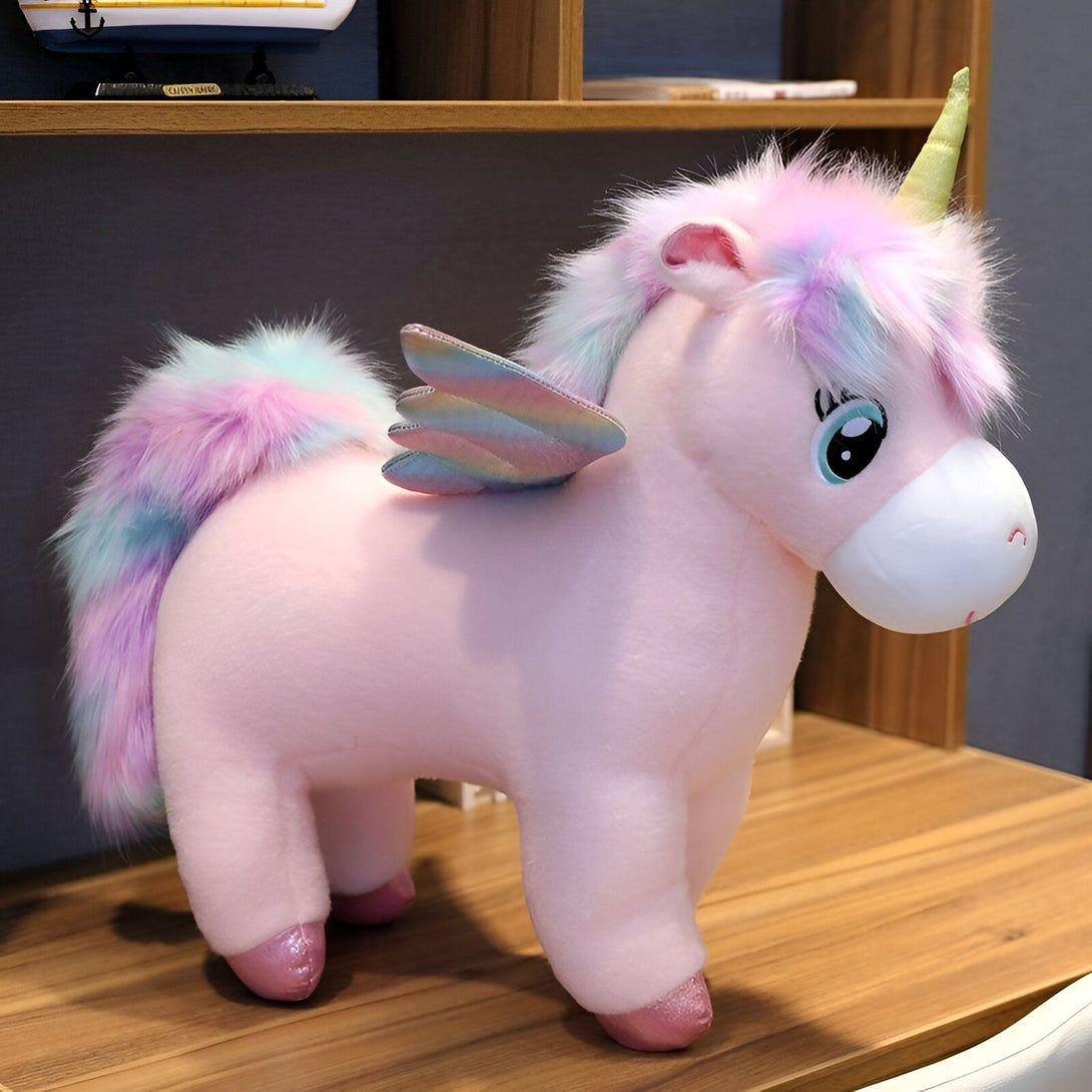 Une peluche licorne rose avec des ailes arc-en-ciel et une crinière et une queue multicolores.