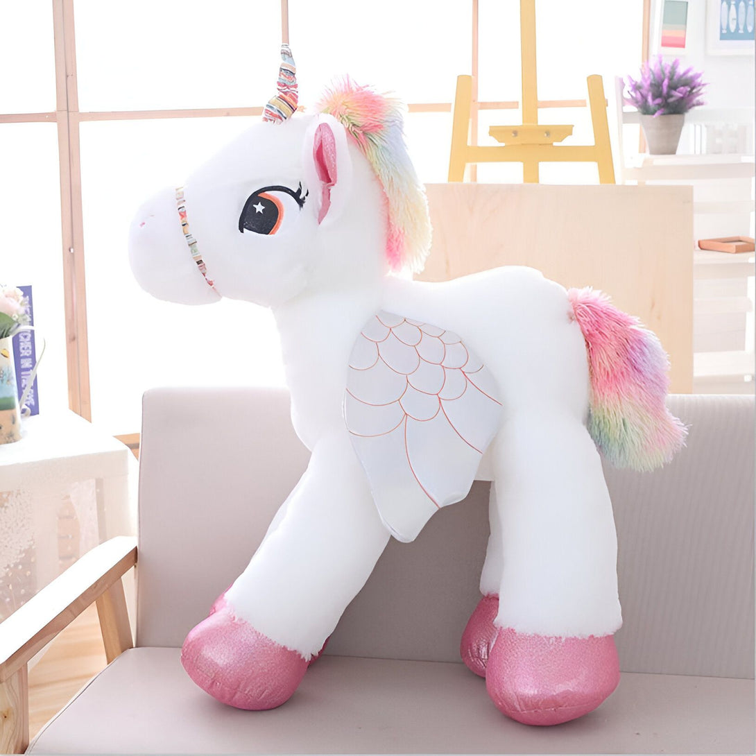 Une peluche licorne blanche avec des ailes et une crinière arc-en-ciel.