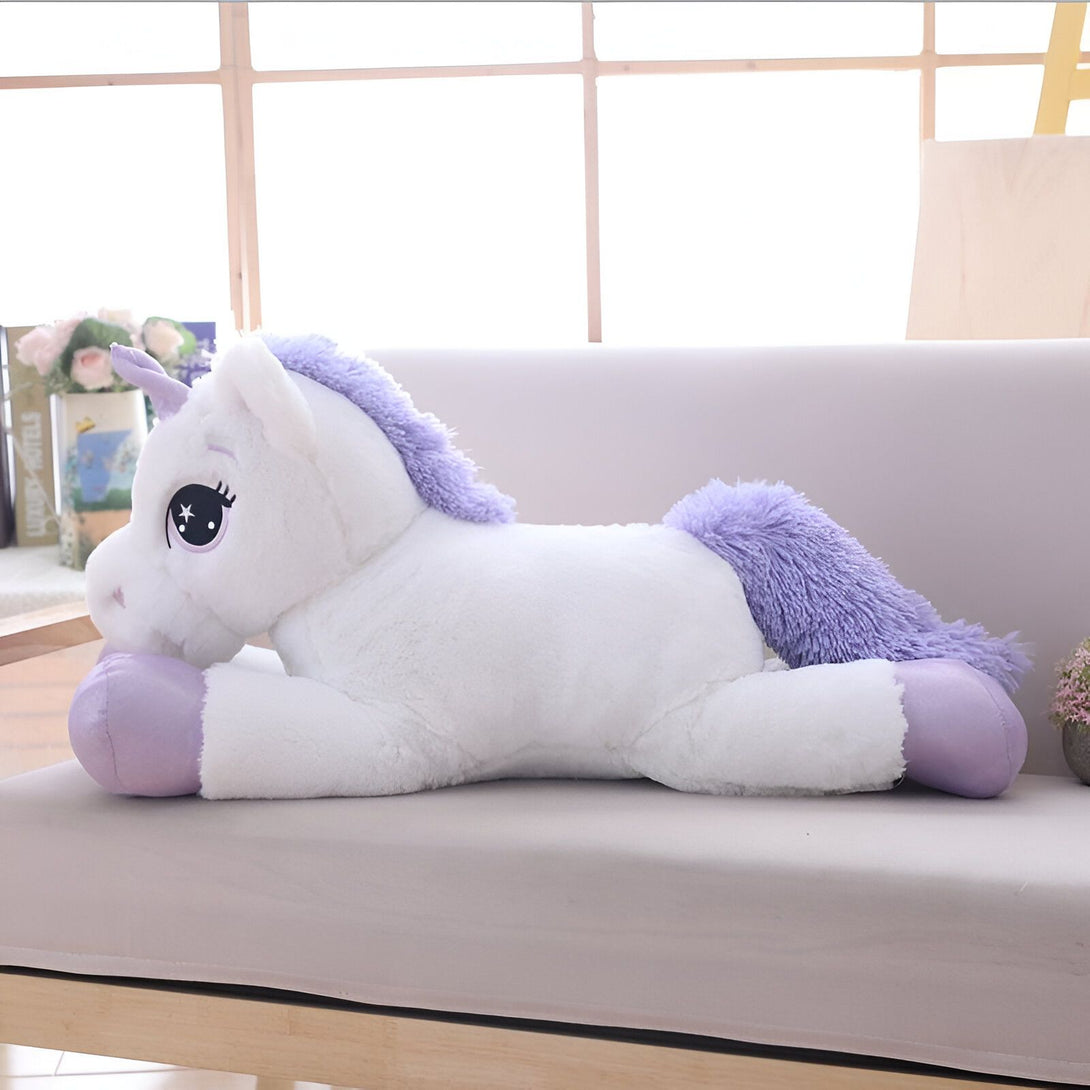 Une peluche géante de licorne blanche et violette allongée sur un canapé.