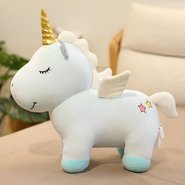 Une peluche licorne blanche avec une crinière et une queue roses, des étoiles et des ailes dorées.