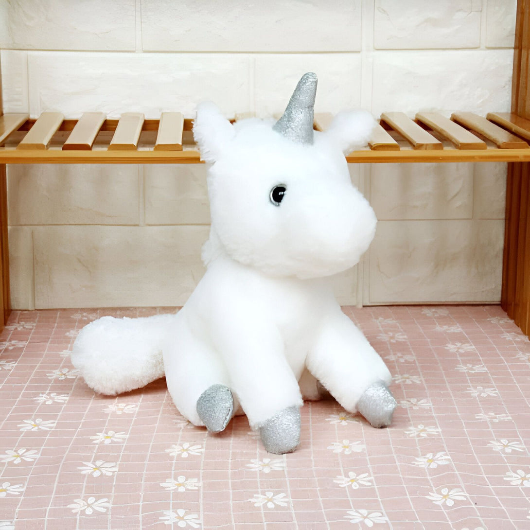Peluche licorne blanche avec corne et sabots argentés. Jouet doux posé sur une surface à motifs floraux devant une étagère en bois., 45501421650175 | Licorne Shop