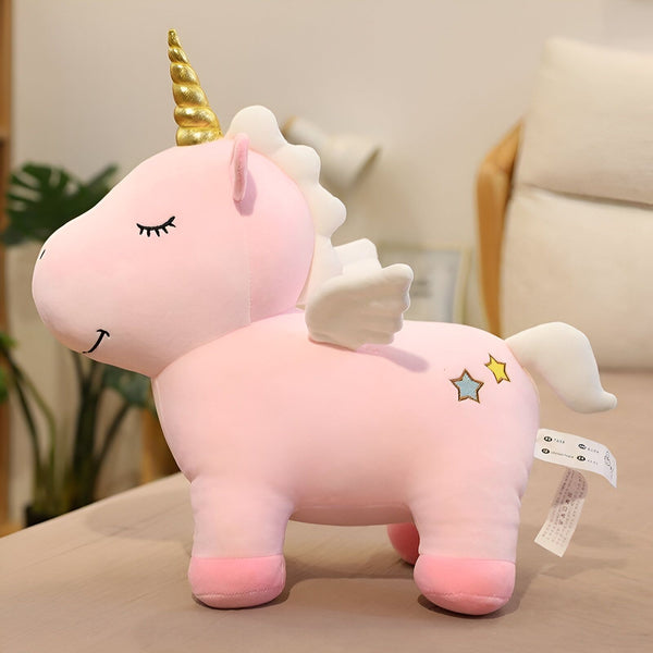 Une peluche licorne rose avec une crinière et une queue blanches, des étoiles bleues et jaunes sur la hanche, des ailes blanches et une corne dorée.