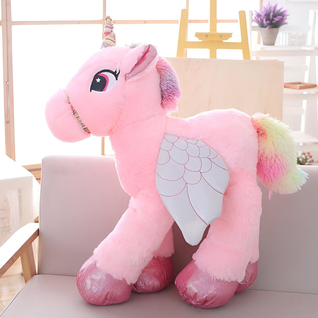 Une peluche licorne rose avec des ailes argentées et une crinière et une queue arc-en-ciel.