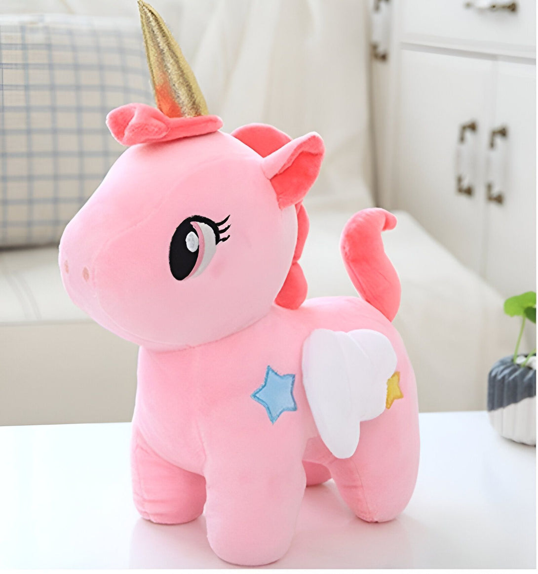 Une peluche rose en forme de licorne avec une corne dorée, des ailes blanches et des étoiles colorées.