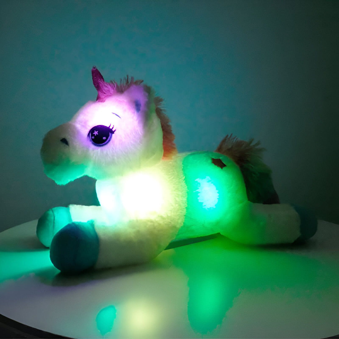 Peluche licorne blanche illuminée par des lumières colorées vives, notamment du vert et du blanc. Les yeux de la licorne sont ornés d'étoiles. La crinière est de couleur pêche. La licorne est couchée sur une surface claire., 45501421289727 | Licorne Shop