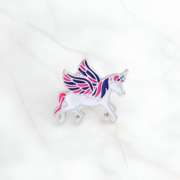 Broche émaillée représentant une licorne blanche avec des ailes bicolores (rose et bleu marine). Détails argentés. Style enfantin et fantaisie. Accessoire de mode original., 45501794550015 | Licorne Shop