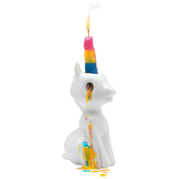Photographie d'une bougie en forme de licorne blanche. La bougie, qui sert de corne, est multicolore et brûle, laissant couler de la cire colorée sur le corps de la licorne., 45501141844223 | Licorne Shop