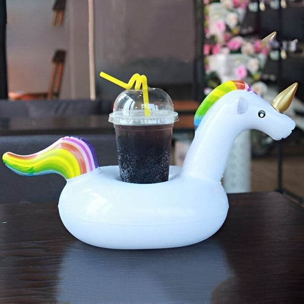 Un verre de soda, avec des pailles jaunes, posé dans un porte-gobelet gonflable en forme de licorne blanche avec une crinière et une queue arc-en-ciel., 45501227598079 | Licorne Shop