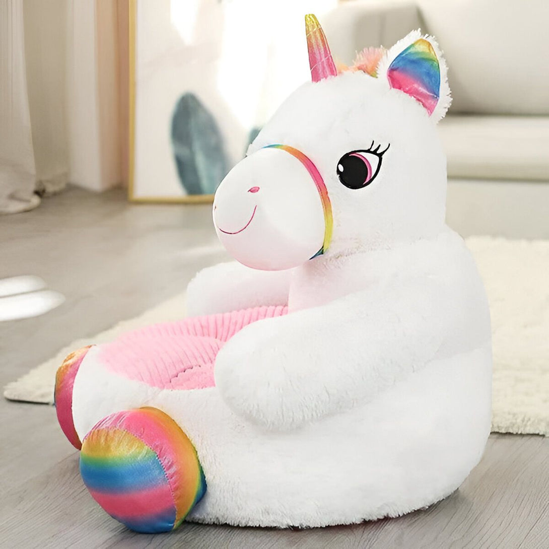 Une peluche licorne blanche et rose avec une crinière et une queue arc-en-ciel. Elle est assise sur un sol beige dans un salon.