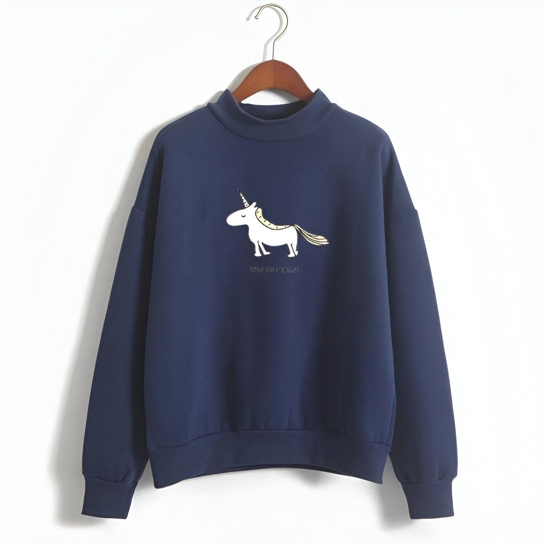 Une image d'un sweat-shirt bleu marine avec une illustration d'une licorne blanche et dorée. La licorne a une crinière et une queue dorées, et porte un collier avec un pendentif en forme de cœur. Le sweat-shirt a un col montant et des manches longues.