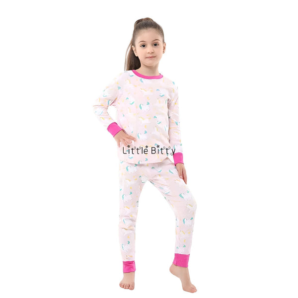 Une fillette porte un pyjama rose à motifs de licornes, avec des bordures rose vif au cou, aux poignets et aux chevilles. Ses cheveux bruns sont attachés en queue de cheval haute., 45502369923327,45502369956095,45502369988863,45502370021631,45502370054399,45502370087167,45502370119935,45502370152703 | Licorne Shop