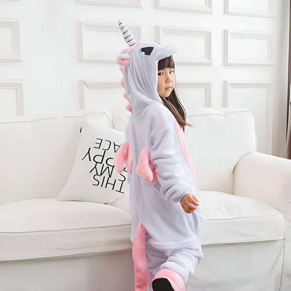 Petite fille portant un pyjama d'hiver en forme de licorne. La combinaison de pyjama est blanche et rose. Elle a une capuche avec une corne de licorne et des oreilles roses., 45501983293695,45501983326463,45501983359231,45501983391999,45501983424767,45501983457535,45501983490303,45501983523071 | Licorne Shop