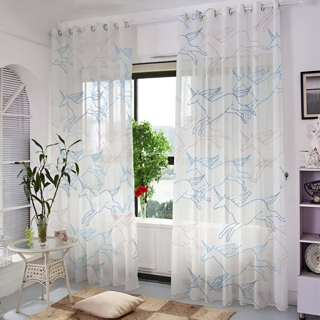 Rideaux blancs transparents avec motifs d'unicorne bleus et roses. Décoration intérieure lumineuse et aérée. Table en rotin et coussin sur tapis tissé. Fenêtre avec vue sur la verdure., 45501076537599 | Licorne Shop
