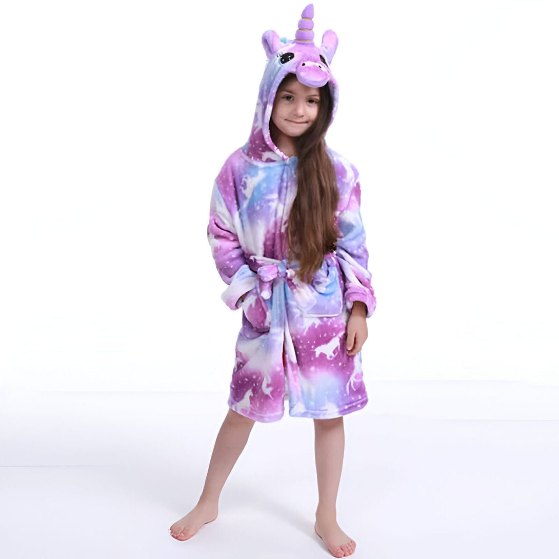 Une jeune fille souriante porte un peignoir en forme de licorne avec une capuche et des motifs d'étoiles violettes et bleues., 45502037688575,45502037852415,45502037983487,45502038081791,45502038212863,45502038311167,45502038343935,45502038376703 | Licorne Shop