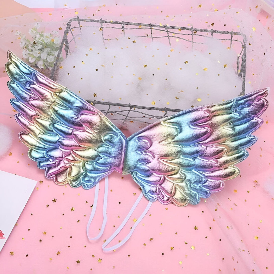 Une paire d'ailes d'ange arc-en-ciel avec des détails en paillettes. Les ailes sont faites d'un matériau léger et iridescent qui reflète la lumière. Elles sont attachées par des rubans blancs qui se nouent autour du cou et du dos. Les ailes sont parfaites pour un costume de fée, de princesse ou de papillon.