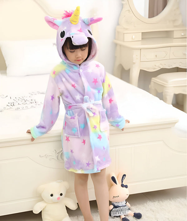 Une petite fille porte un peignoir licorne coloré avec des étoiles, debout près d'un lit avec des jouets., 45502344986879,45502345019647,45502345052415,45502345085183,45502345117951,45502345150719,45502345183487,45502345216255 | Licorne Shop