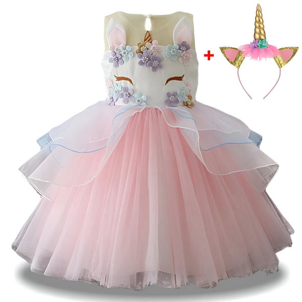 Une robe de licorne rose et blanche avec des fleurs et une licorne sur le devant. La robe est en tulle et a plusieurs couches. Il y a aussi un serre-tête avec une licorne.