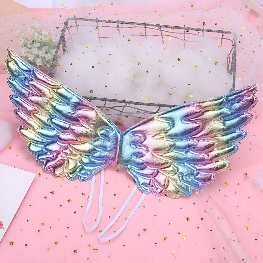 Une paire d'ailes d'ange arc-en-ciel avec des paillettes. Les ailes sont faites d'un tissu irisé et ont des détails en paillettes. Elles sont attachées par des rubans blancs.