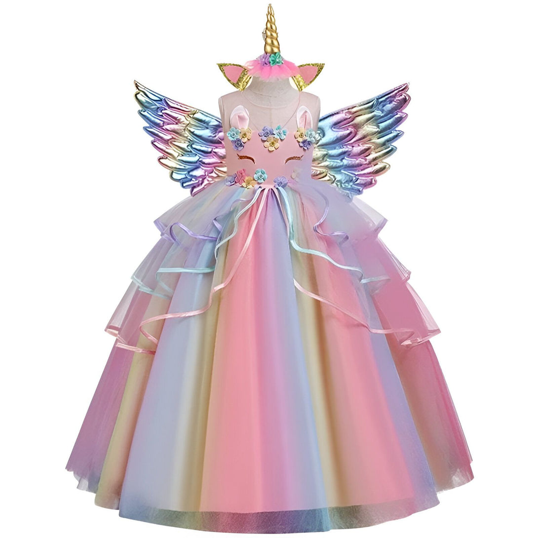 Une petite fille porte une robe de licorne rose et blanche. La robe est ornée de fleurs et de paillettes. La petite fille a des ailes de licorne et une couronne de fleurs sur la tête.