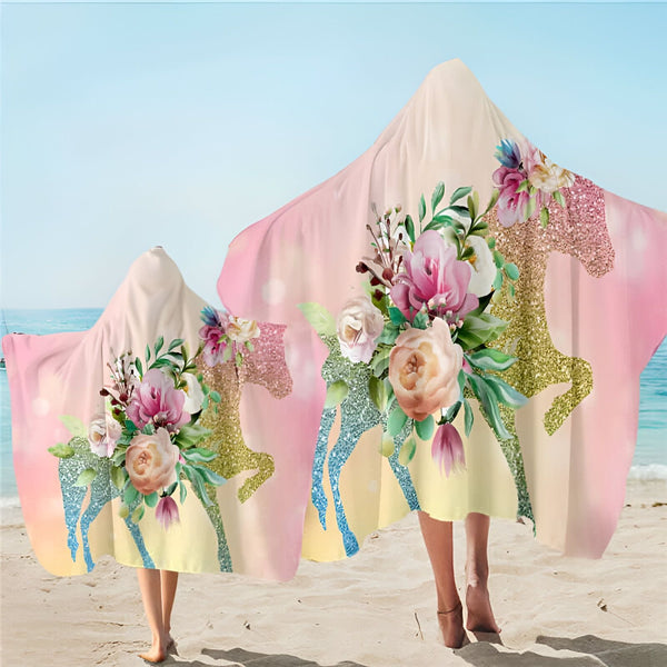 Deux personnes sur une plage, portant des serviettes à capuche imprimées de motifs floraux et de licornes pailletées. Couleurs dominantes : rose, jaune et bleu., 45501254762751 | Licorne Shop