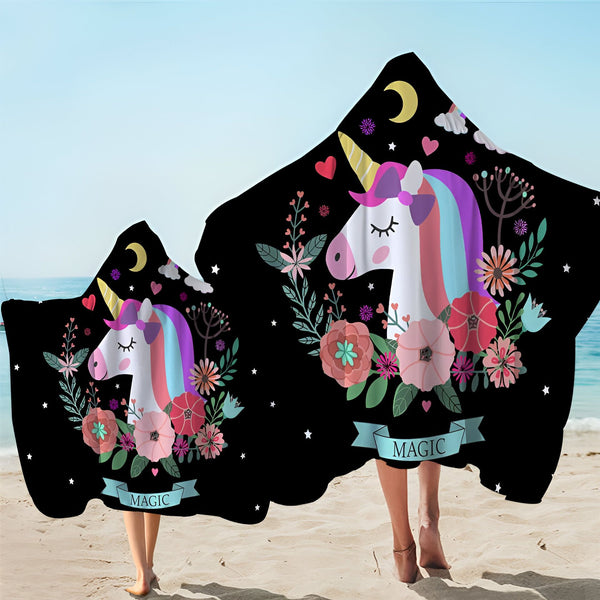 Deux personnes sur une plage portant des serviettes poncho à capuche noires décorées d'une illustration de licorne, de fleurs, d'étoiles, de lunes et du mot « Magic »., 45501227073791 | Licorne Shop