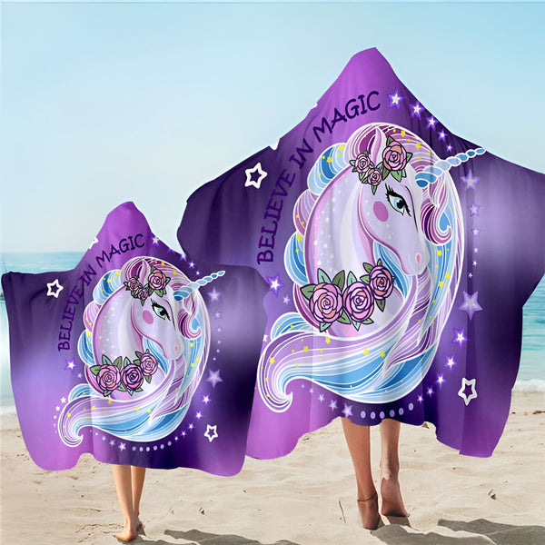 Deux personnes sur la plage, portant des serviettes à capuche violettes avec une illustration de licorne, entourée de roses et d'étoiles, et l'inscription "Believe in magic" (Croyez à la magie)., 45501253910783 | Licorne Shop