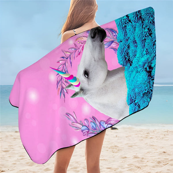 Femme sur la plage enveloppée dans une serviette de plage à motif de tête de licorne blanche avec une corne colorée, des fleurs et des feuilles sur un fond rose et des fleurs bleues., 45501251944703 | Licorne Shop