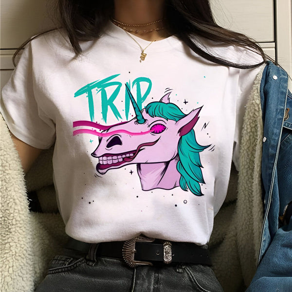 Une image d'une femme portant un t-shirt blanc avec un imprimé d'une licorne effrayante. La licorne a une crinière verte et des yeux rouges. Le texte "TRIP" est écrit en lettres roses et bleues au-dessus de la licorne.