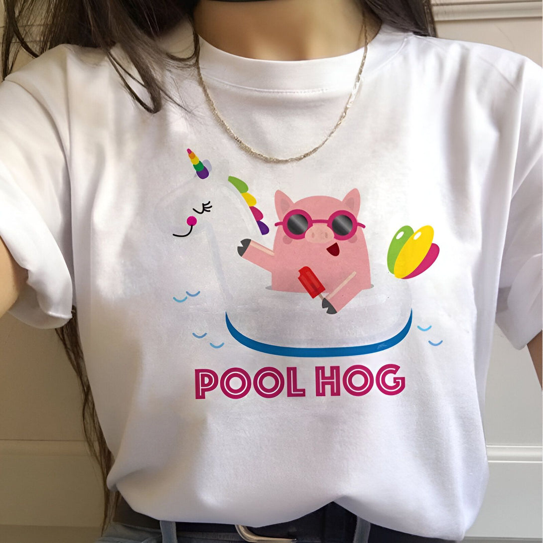 Une image d'un t-shirt blanc avec un motif d'un cochon rose avec des lunettes de soleil et une licorne qui flottent sur une bouée dans une piscine. Le texte "Pool Hog" est écrit en rose sous le motif.