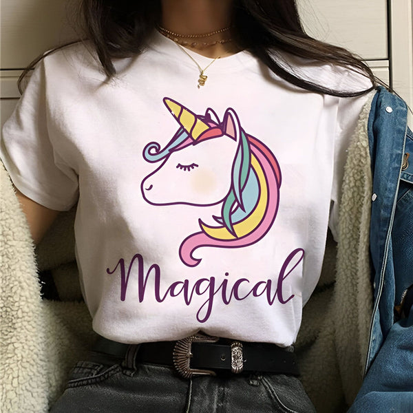 Une jeune femme porte un t-shirt blanc avec un motif de licorne. La licorne a une corne dorée, une crinière et une queue arc-en-ciel. Le texte "Magical" est écrit en violet sous la licorne.