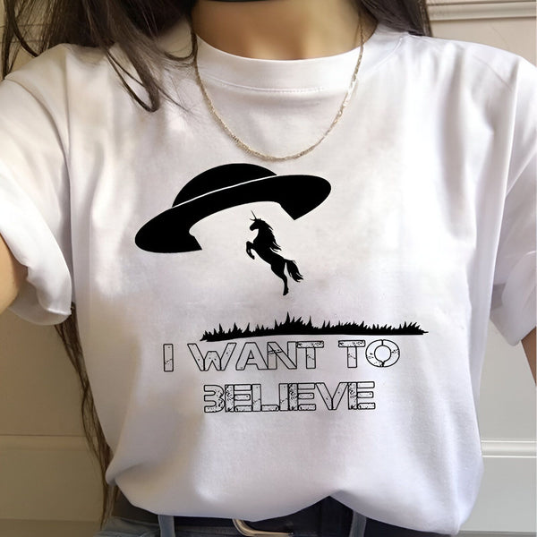 Le texte "I want to believe" est écrit en anglais sur un t-shirt blanc. Au-dessus du texte, on peut voir une soucoupe volante noire avec un cheval ailé.