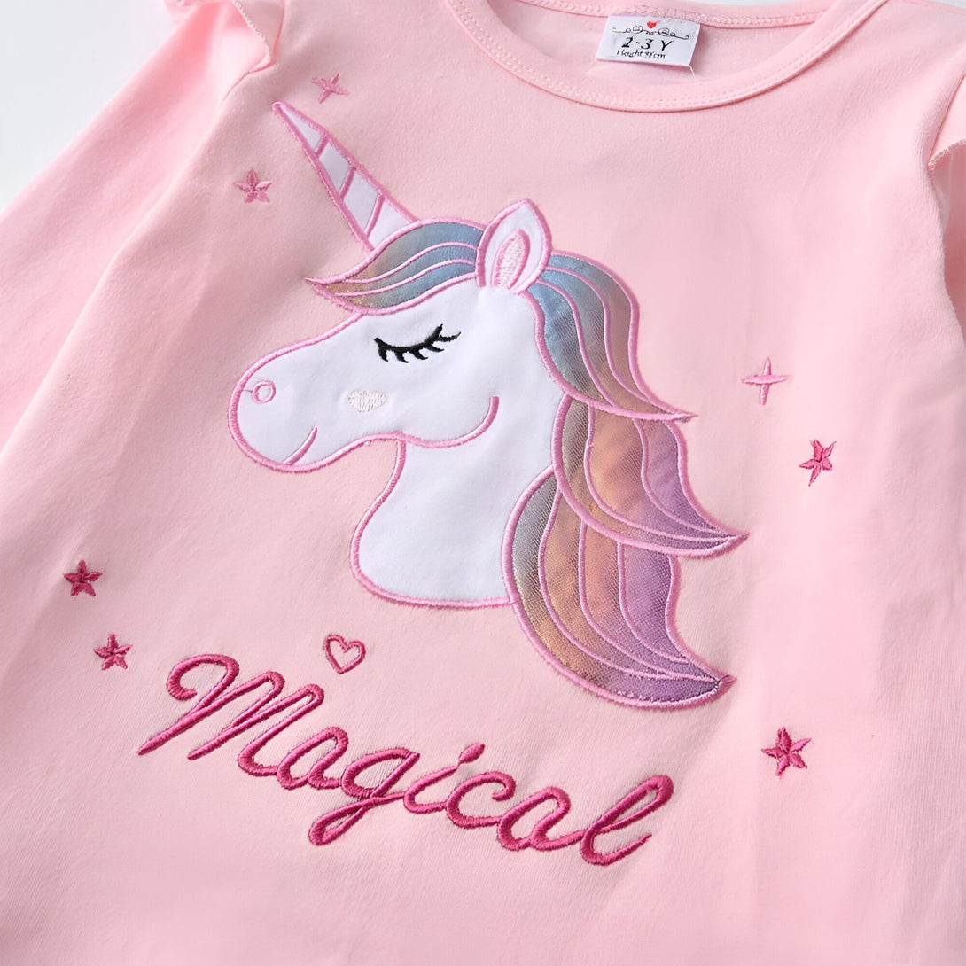 Une image d'une licorne magique brodée sur un t-shirt rose pour enfant. La licorne a une crinière et une queue arc-en-ciel, et il y a des étoiles roses et blanches autour d'elle. Le texte "Magical" est brodé en dessous de la licorne.