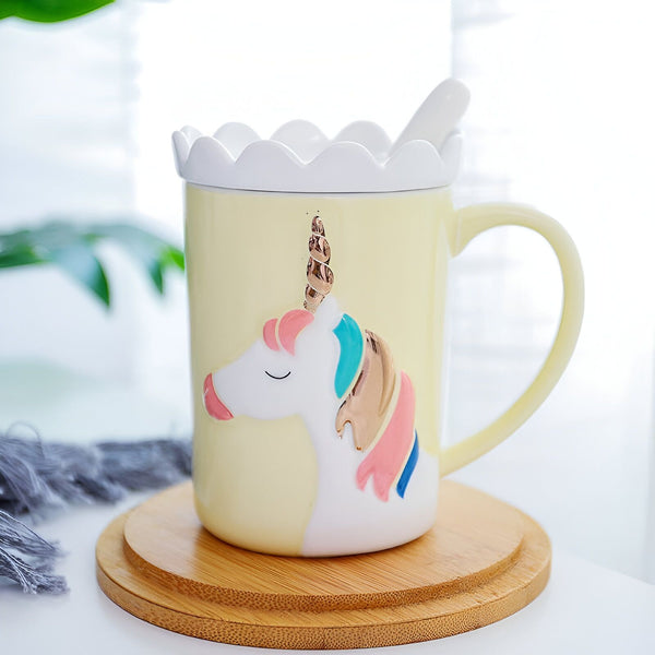 Tasse jaune pâle avec couvercle décoré et motif licorne en relief. Une cuillère blanche repose sur le couvercle. Le tout est posé sur un sous-plat en bois., 45501199483135 | Licorne Shop