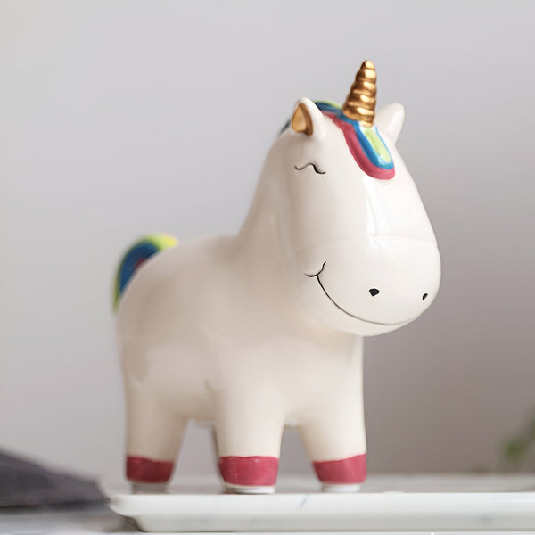 Une figurine de licorne en céramique blanche avec une corne dorée, une crinière et une queue arc-en-ciel et des sabots roses.