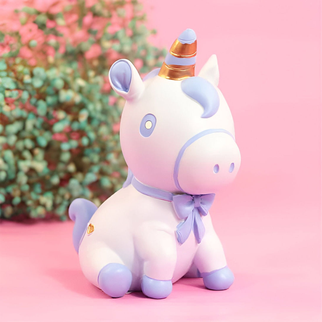 Figurine décorative d'un licorne blanc assis avec des détails lilas, un noeud papillon et une corne dorée, sur un fond rose et fleuri., 45501183656191 | Licorne Shop