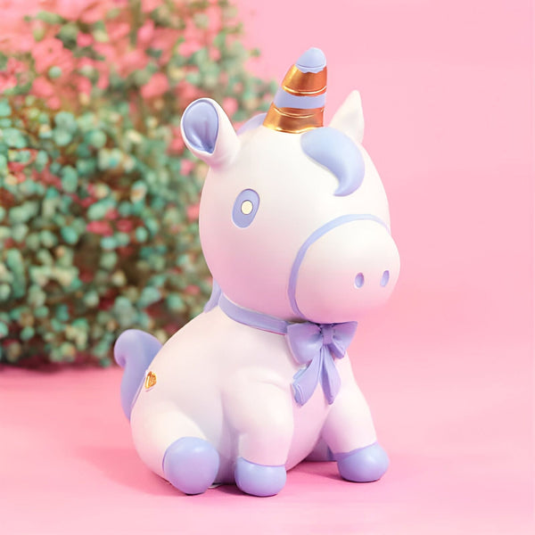 Figurine décorative d'un licorne blanc assis avec des détails lilas, un noeud papillon et une corne dorée, sur un fond rose et fleuri., 45501183656191 | Licorne Shop